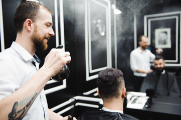 Fototapeta premium Young handsome barber making haircut of attractive man in barbershop