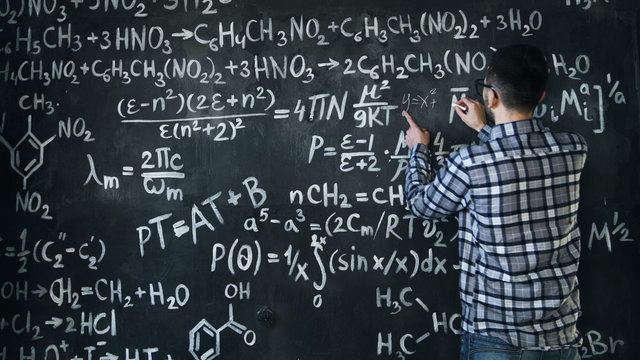 Young scientist man write chock in chemical and mathematical equations wall room interior