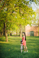 Cath the moment. Young woman in a pink dress with a bike with flowers in a summer park. Family vacations. Europe tradition.