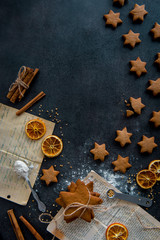 Top view of food preparation. Star shaped gingerbread cookies arranged in shape of shooting star and ingredients (cinnamon sticks, dried orange slices, flour) on dark modern kitchen table from above.