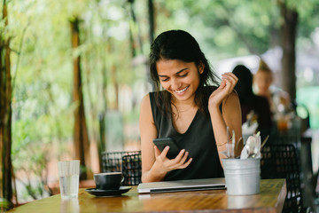 Young Indian woman looking at her smartphone in a cafe in sunlight