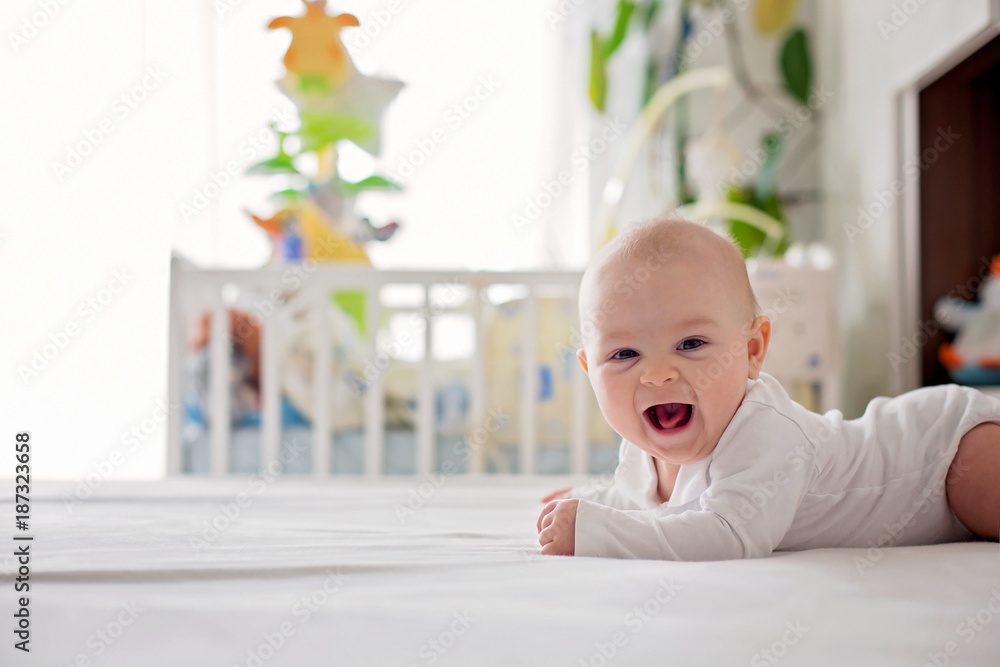 Wall mural cute little four month old baby boy, playing at home in bed in bedroom, soft back light