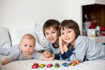 Three children, baby and his older brothers in bed in the morning, playing together