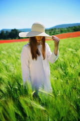 Young girl wearing a hat in a white dress in a green wheat field, freedom, life, joy, unity with nature