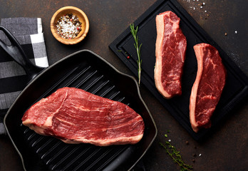 Raw fresh meat Picanha steak, traditional Brazilian cut with thyme, garlic, and black pepper on wooden board. Sliced meat Black Angus steak on grill iron pan. Top view.