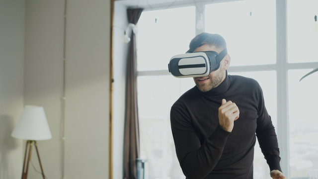 Excited Young Man With Virtual Reality Headset Dancing And Play 360 Video Game At Home