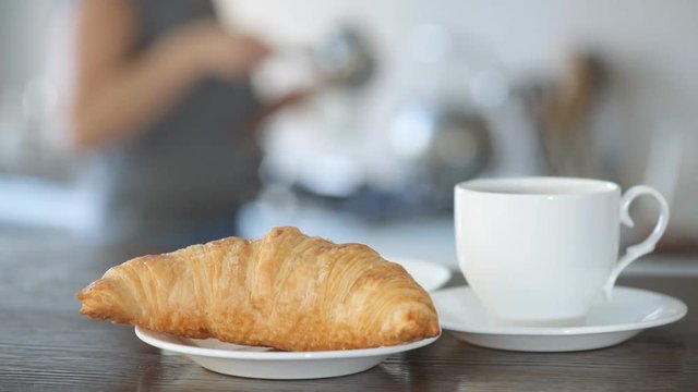 Young woman pours coffee into a cup .  Steam from a cup with a hot coffee with croissant . Healthy breakfast.