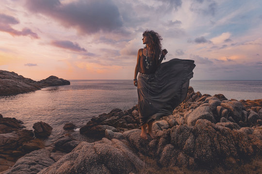 beautiful woman on the top of the rock at sunset over sea background