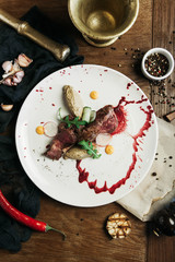 restaurant dish Grilled meat with berry sauce, with a pepper mortar and pestle on a wooden table