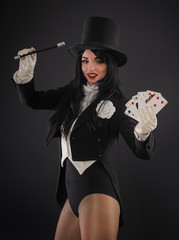 Female magician in performer suit with magic wand and playing cards