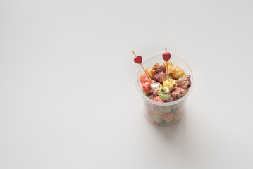 Still-life of festive multicolored popcorn on Valentine's day with colorful popcorn and two red hearts on white background