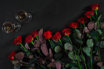 Bouquet of red roses and two glasses of champagne on a black bac