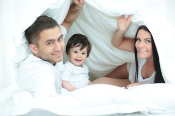 Happy family posing under a duvet while looking at the camera