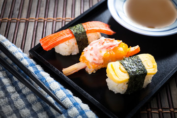 Close up Sushi set with chopsticks and soy on black plate and bamboo background.