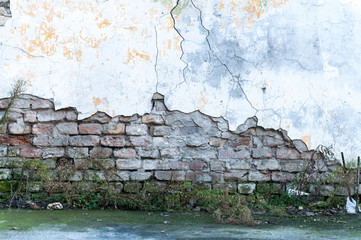 Old damaged brick wall with bad foundation and peeled plaster almost collapsed