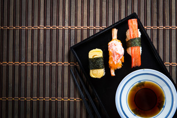 Close up Sushi set with chopsticks and soy on black plate and bamboo background.