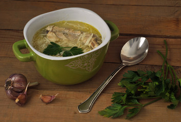 Chicken noodle soup in a ceramic bowl, garlic and greens on a wooden table. 