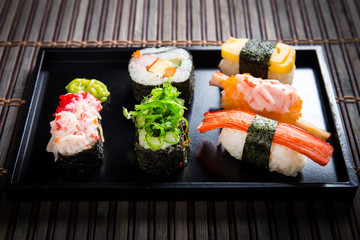 Close up Sushi set with chopsticks and soy on black plate and bamboo background.