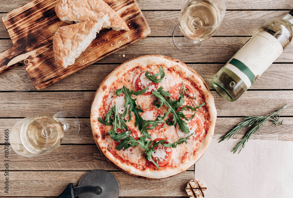 Wall mural italian pizza margherita with arugula, with a bottle and two glasses of white wine on a wooden table