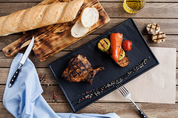 juicy steak and grilled vegetables on a black board, with bread on a wooden table