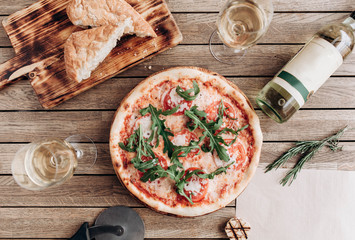 Italian pizza margherita with arugula, with a bottle and two glasses of white wine on a wooden table - 187334685