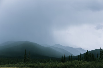 Rain shows layers of mountains. A misty scene with multiple mountains with green tones and greys.