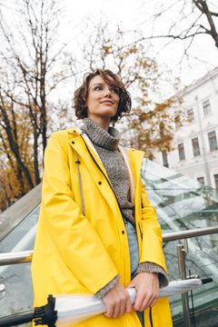 Brunette woman with bob haircut wearing glasses and yellow raincoat exploring landmarks in touristic place