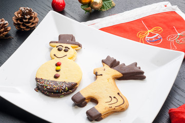 Biscotti di pasta frolla a forma di pupazzo di neve e di renna decorati su un piatto