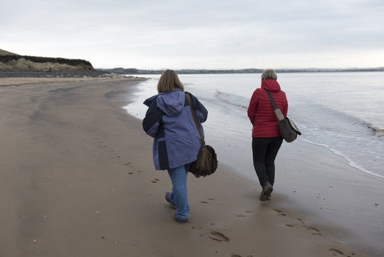 Rear view image of a mature female couple walking along the beach on a cold day 
