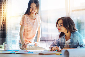 Obraz premium Our project. Positive delighted joyful students smiling and looking at each other while studying together