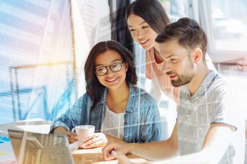Office team. Nice smart young people smiling and looking at the laptop screen while working together in the office