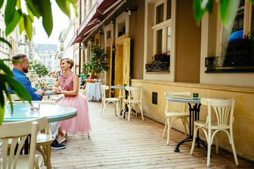 Romantic fashionable couple having great time together. Bride and groom sitting in cafe terrace outdoor.