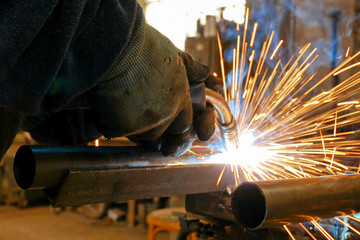 Worker Welds Iron Pipe in the Workroom.