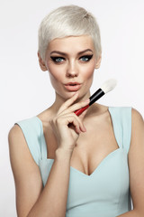 Fototapeta premium Young beautiful tanned woman with stylish cat eye make-up and platinum blonde hair holding makeup brush