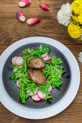 Warm salad with chicken liver, arugula and radish with sauce on the black plate. Wooden rustic background. Selective focus. Top view