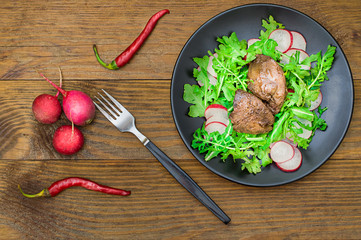 Warm salad with chicken liver, arugula and radish with sauce on the black plate. Wooden rustic background. Selective focus. Top view