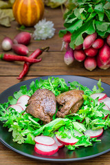 Warm salad with chicken liver, arugula and radish with sauce on the black plate. Wooden rustic background. Selective focus. Top view