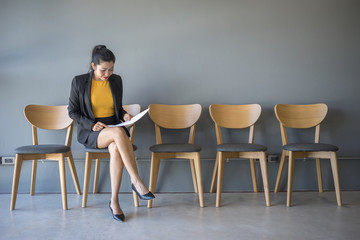 A woman sitting in a chair reading a document while waiting for a job interview in the waiting room.