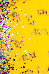 Colorful confetti and golden coiled streamers on yellow background