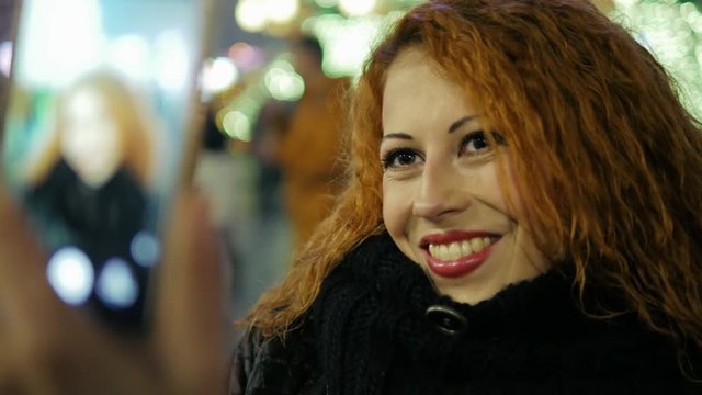 Beautiful curly red hair woman makes   selfie by mobile at city holiday close-up