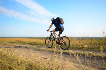 Naklejka premium Male cyclist with backpack driving by rural dirt road outdoors