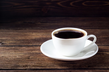 White cup with black coffee on wooden background.