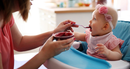 Mother feeding baby with spoon indoors