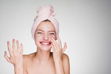 Laughing young girl with a pink towel on her head applying a nourishing cream on her face - 187346238