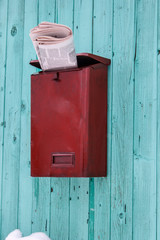 Red mailbox overflowing with newspapers on blue wooden wall