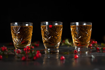 glasses with orange drink and branches with red berries on a dark wet background
