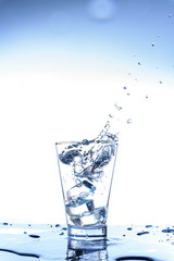 Ice dropping and water splashing in the glass with reflection on the mirror table and isolated on white background.