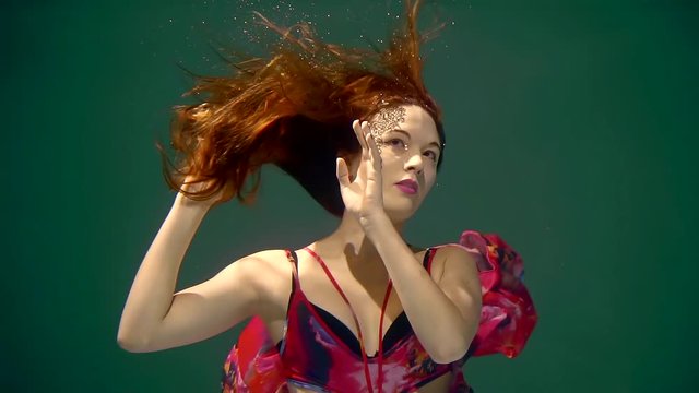 girl with red hair under water with face painting in a beautiful dress