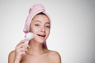 happy smiling woman with pink towel on head cleans face with electric brush