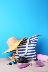 Summer bag with hat, flip flops, camera and starfish on beach sand